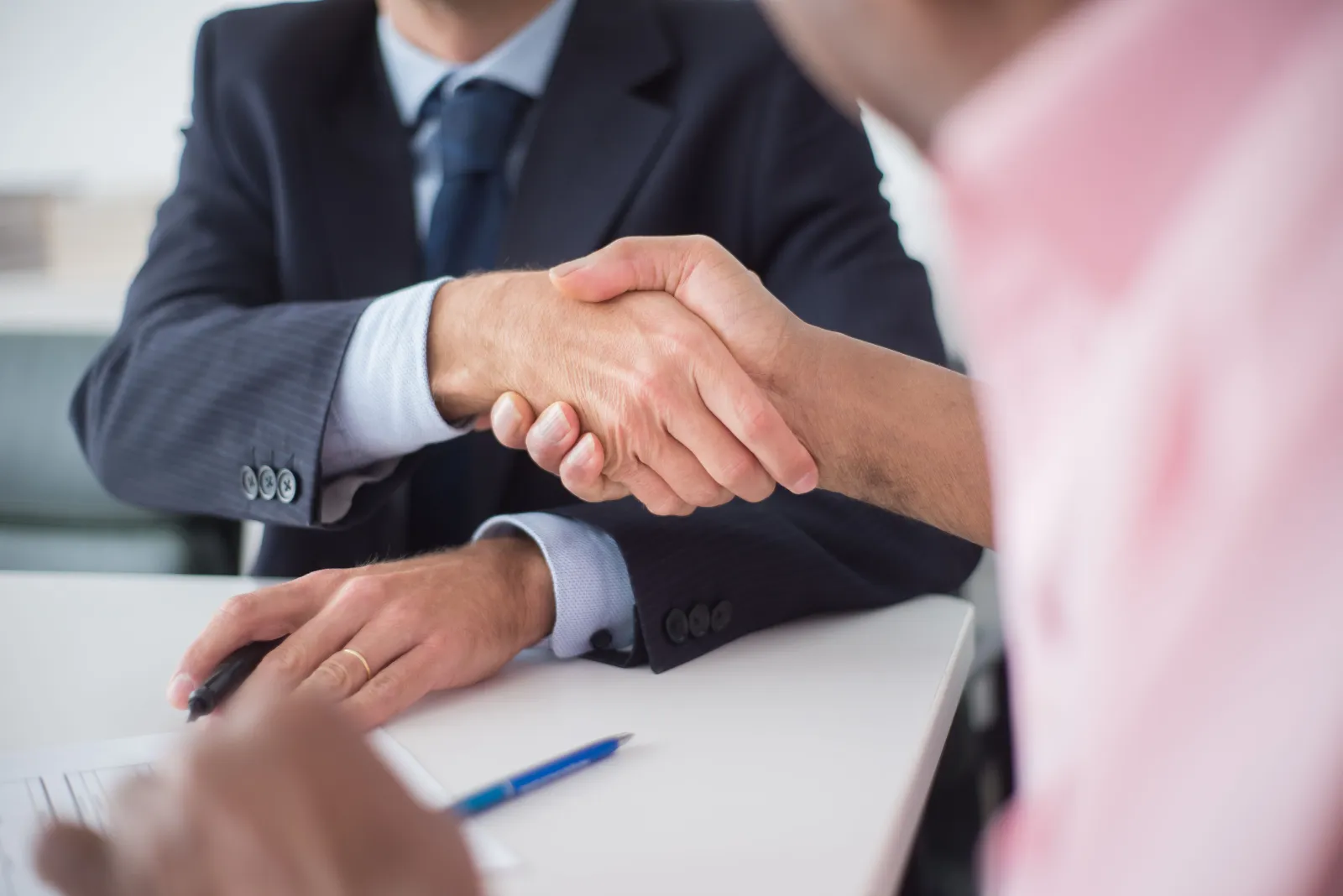 Two people shaking hands across a desk at the end of a meeting