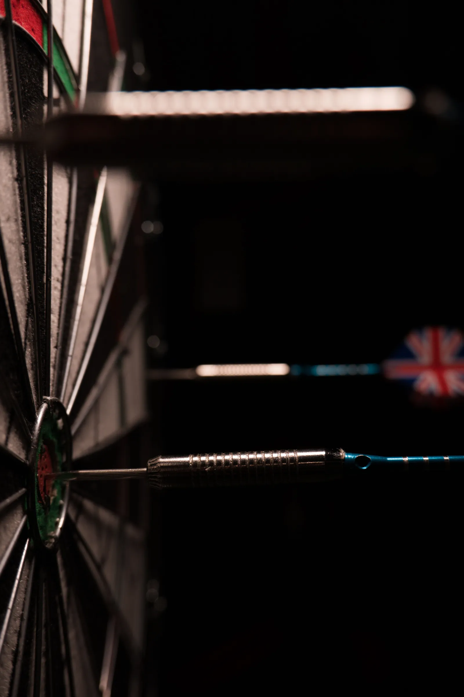 A single dart in the centre of a dartboard, lit against a dark background